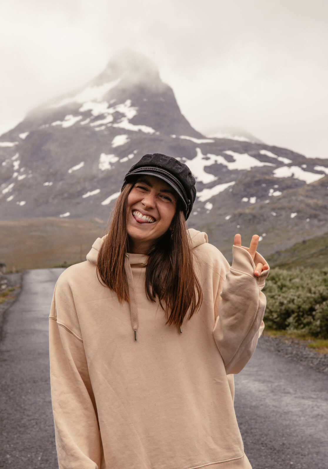 Angie trägt den upgecycelten Hoodie, der in Zusammenarbeit mit Phil und Lui entstanden ist und zeigt das Peace Zeichen, in den Bergen.
