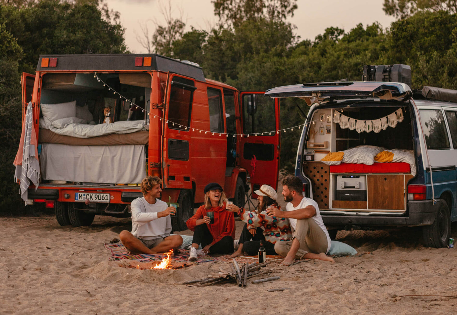 Angie und Sascha sitzen mit ihren Freunden und Vans am Lagerfeuer. 